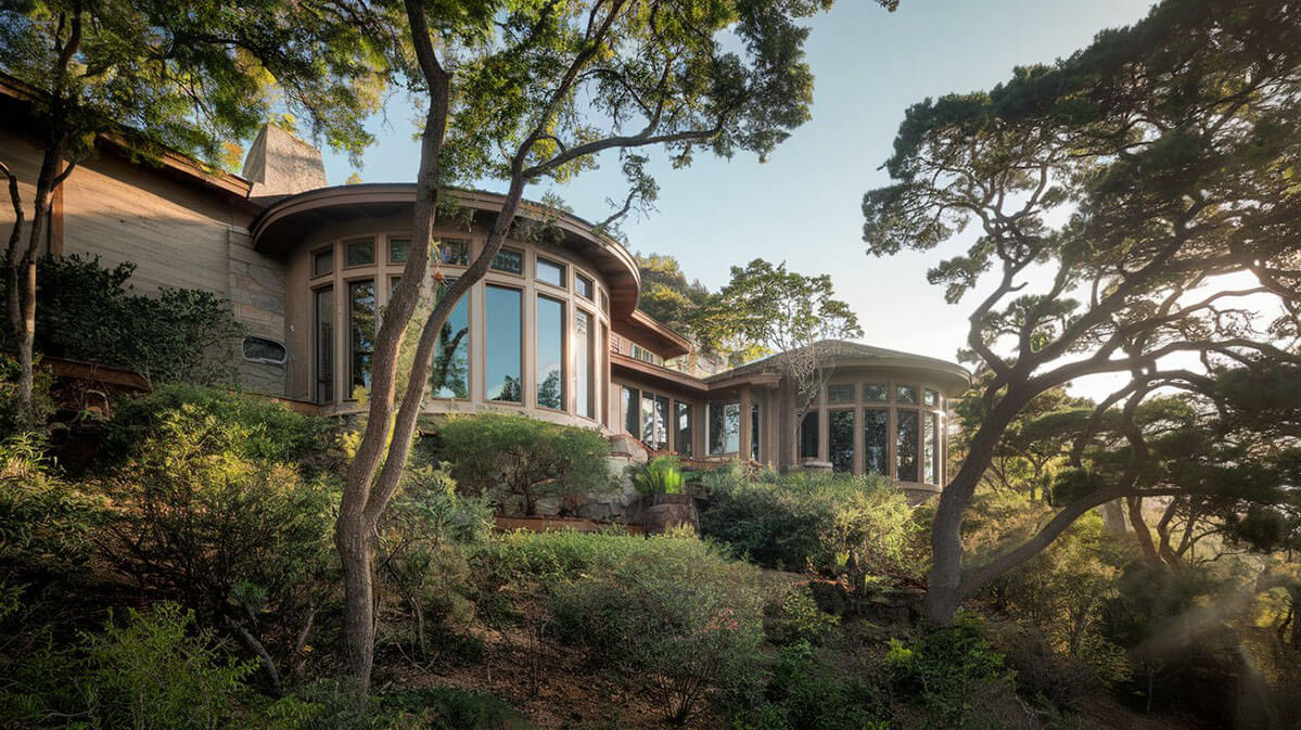 Hillside Home Amid Nature A hillside home with round windows, surrounded by greenery and tall trees, blending seamlessly with nature, example of nature design